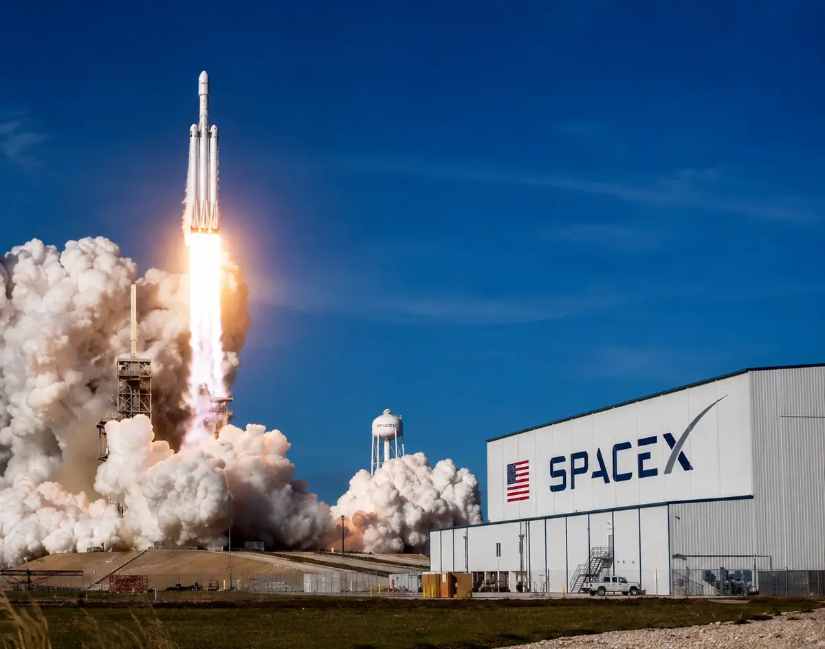 SpaceX rocket launching from a launchpad near a SpaceX facility with large clouds of smoke and a bright blue sky, representing modern space technology and aerospace innovation.